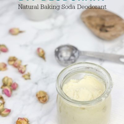 DIY deodorant in a glass jar on a white wash cloth with rose buds to the left and a steel measuring spoon behind it.