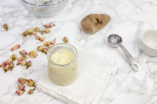 DIY deodorant in a glass jar on a white wash cloth with rose buds around it