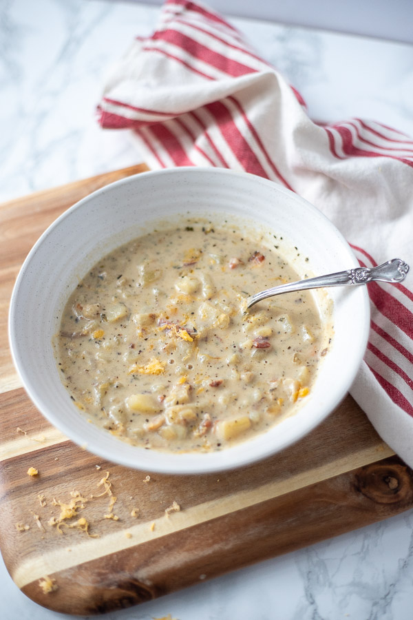 bowl of east potato bacon soup in a cream colored bowl with a spoon in the soup. 