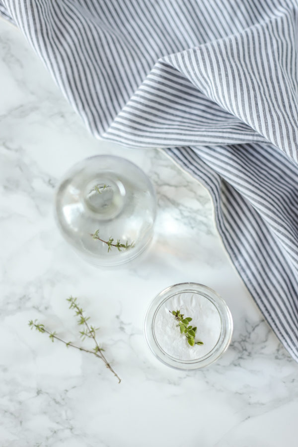 two ingredients to make drain cleaner in glass jars on a marble countertop with fresh herbs