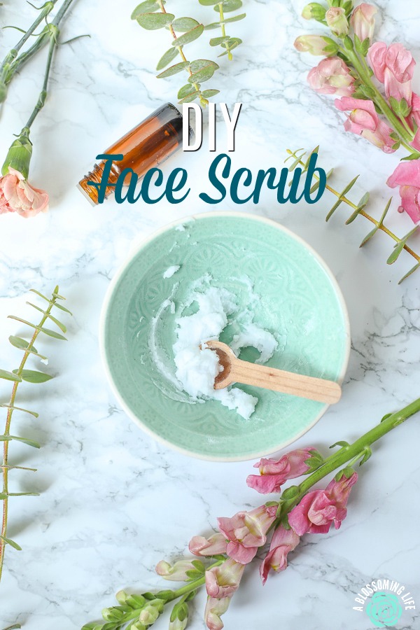 teal bowl of DIY face scrub with a wooden spoon and flowers all around.