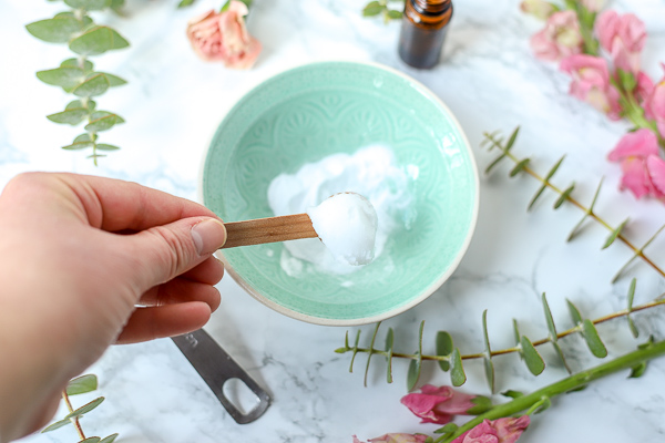 wooden spoon with coconut oil to make DIY Face Scrub in teal bowl