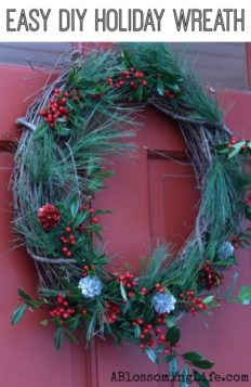 DIY Christmas Wreath with greenery, holly, and pinecones hanging on a red door