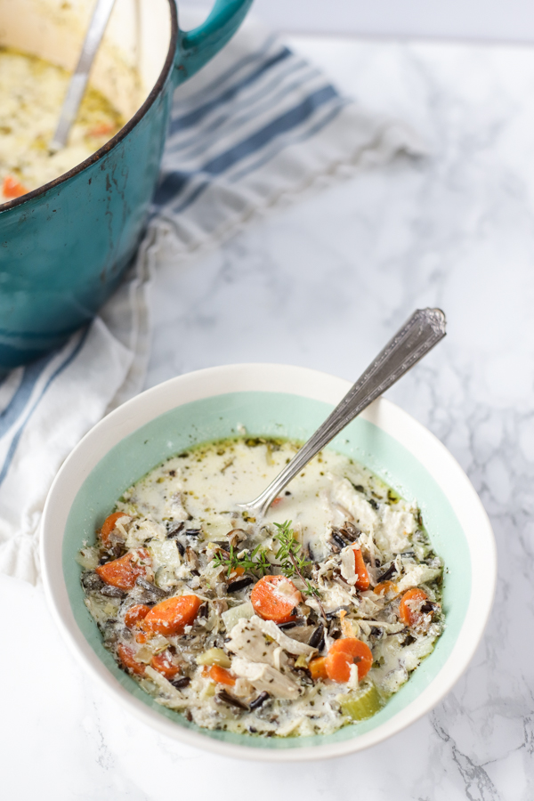 overhead shot of chicken and wild rice soup in a cream and teal bowl with a turquoise dutch oven in the back