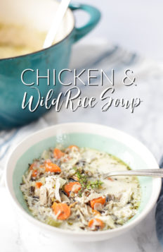 creamy chicken and wild rice soup with carrots, celery, chicken, wild rice and onions in a creamy base and topped with fresh herbs in a cream and teal bowl with a dutch oven behind