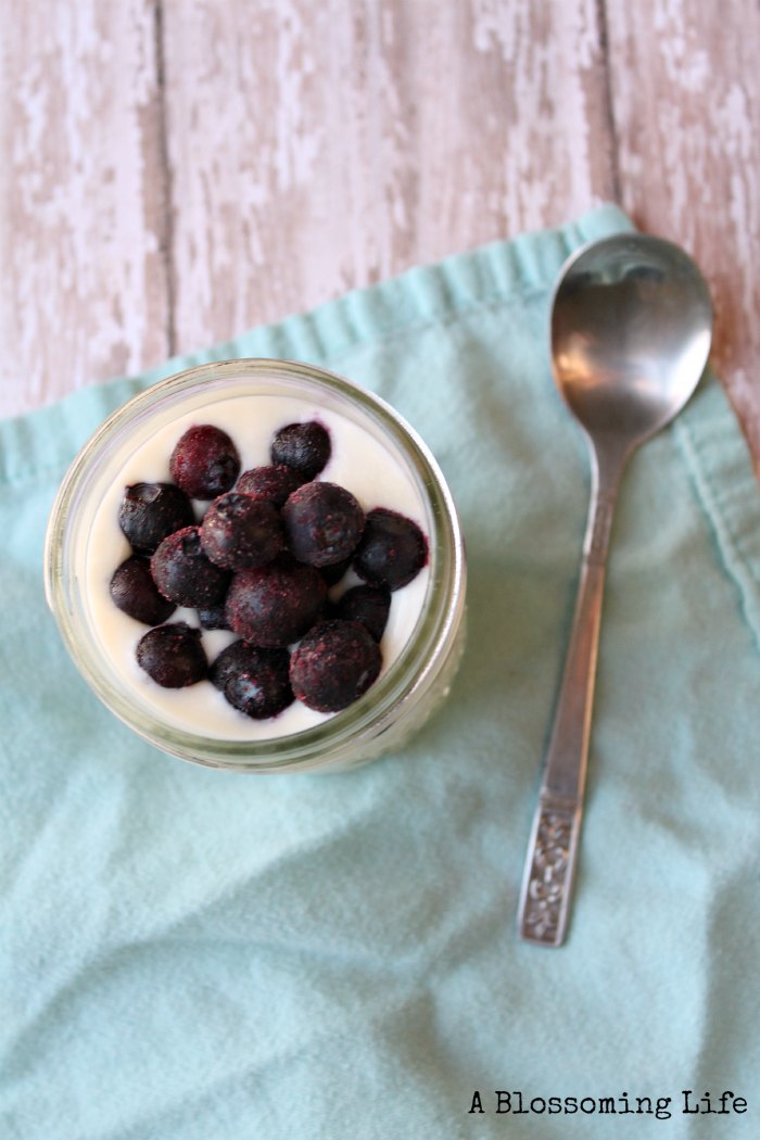 raw milk yogurt in a mason jar with frozen blueberries on top a blue towel with a spoon to the right