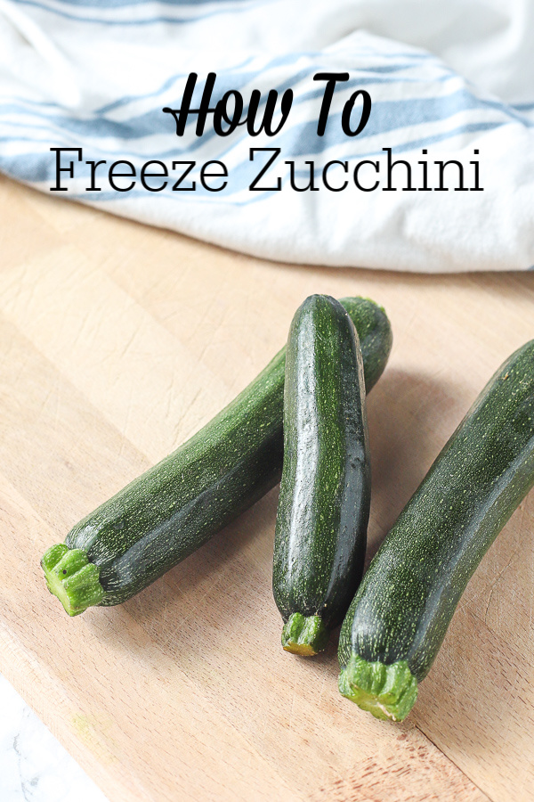 three fresh zucchini laying on a wood cutting board with a blue and white striped napkin behind it