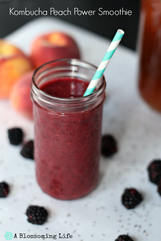 berry peach smoothie in a glass jar with a straw surrounded by peaches and blackberries.