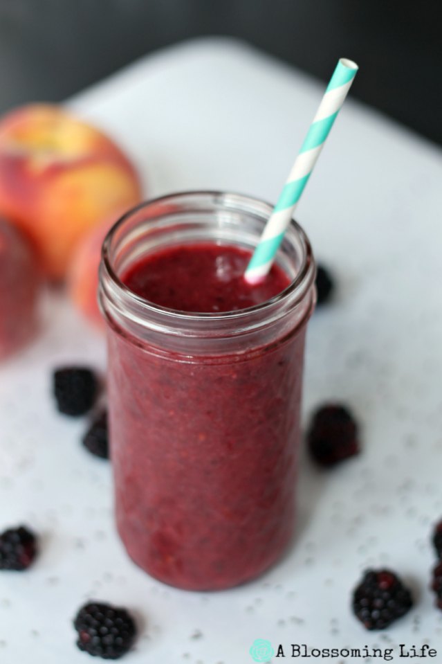 Berry peach smoothie in a glass jar with a teal and white stripe straw in it