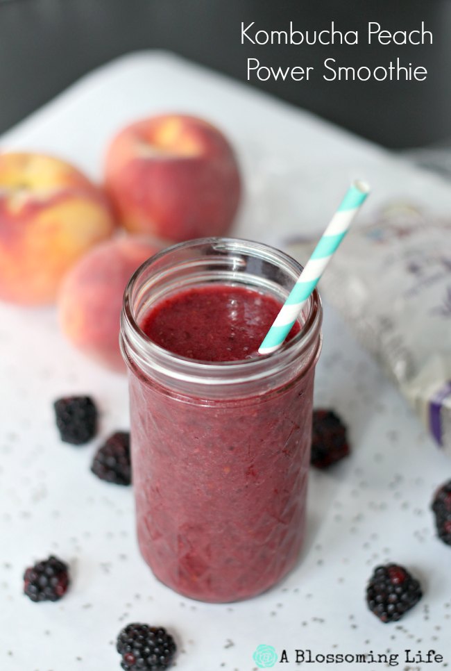 Kombucha berry peach smoothie in a glass mason jar with peaches and blackberries behind it