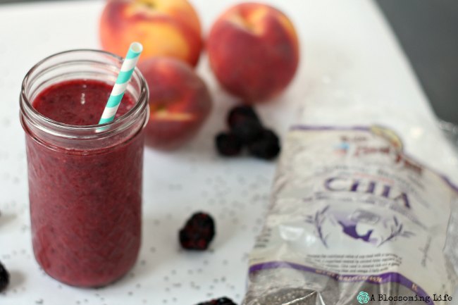 Berry peach Smoothie with Chia Seeds in a glass cup with blackberries, peaches, and chia seeds on a white counter