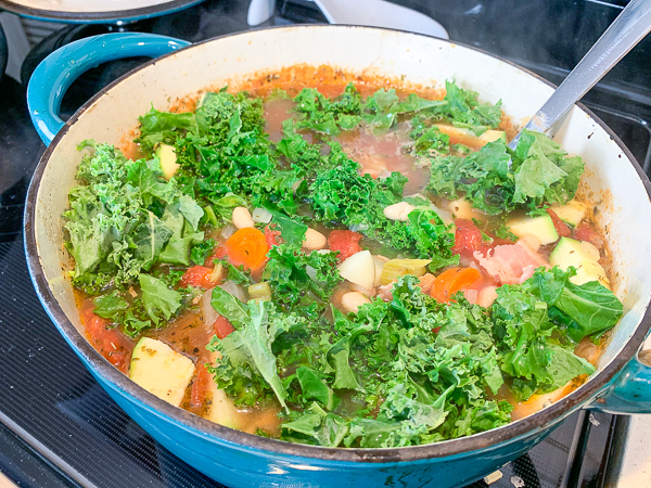 fresh kale and zucchini are added to a dutch oven to make minestrone soup