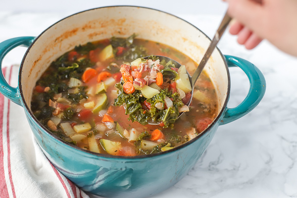 large dutch oven of hearty classic minestrone soup with a ladle ladling out soup