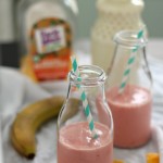 two orange mango smoothies in glass milk jars with straws on a table with ingredients around