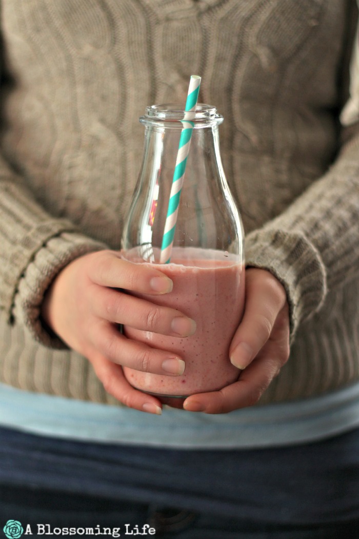 women wearing tan knit sweater holding orange mango smoothie with a straw coming out of the glass