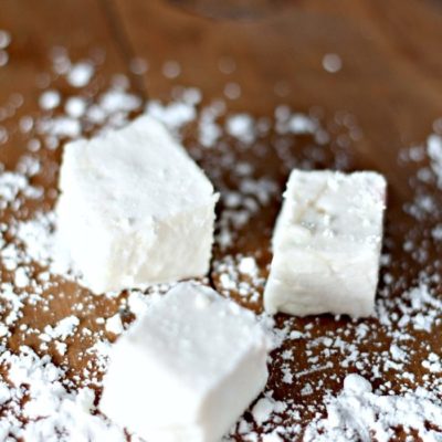 three homemade marshmallows on a wood table with cornstarch sprinkled around