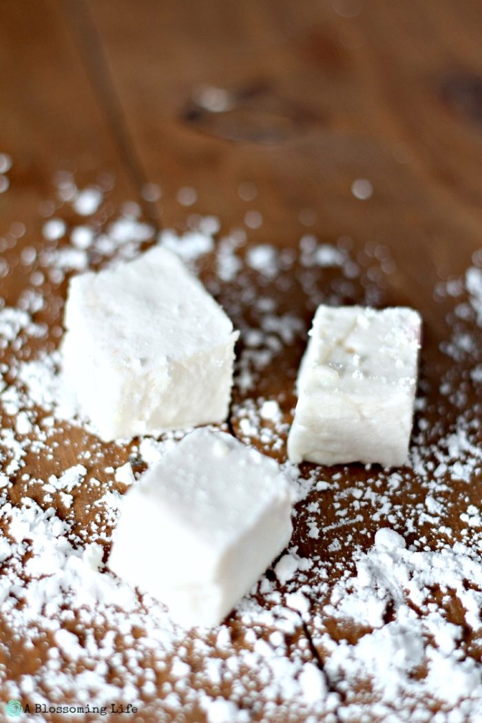 three homemade marshmallows on a wood table with cornstarch sprinkled around