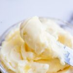 Whipped honey butter being scooped out with a knife from a glass bowl.