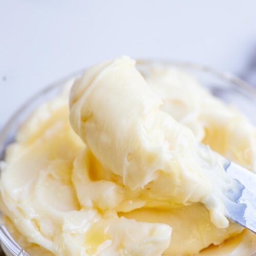 Whipped honey butter being scooped out with a knife from a glass bowl.