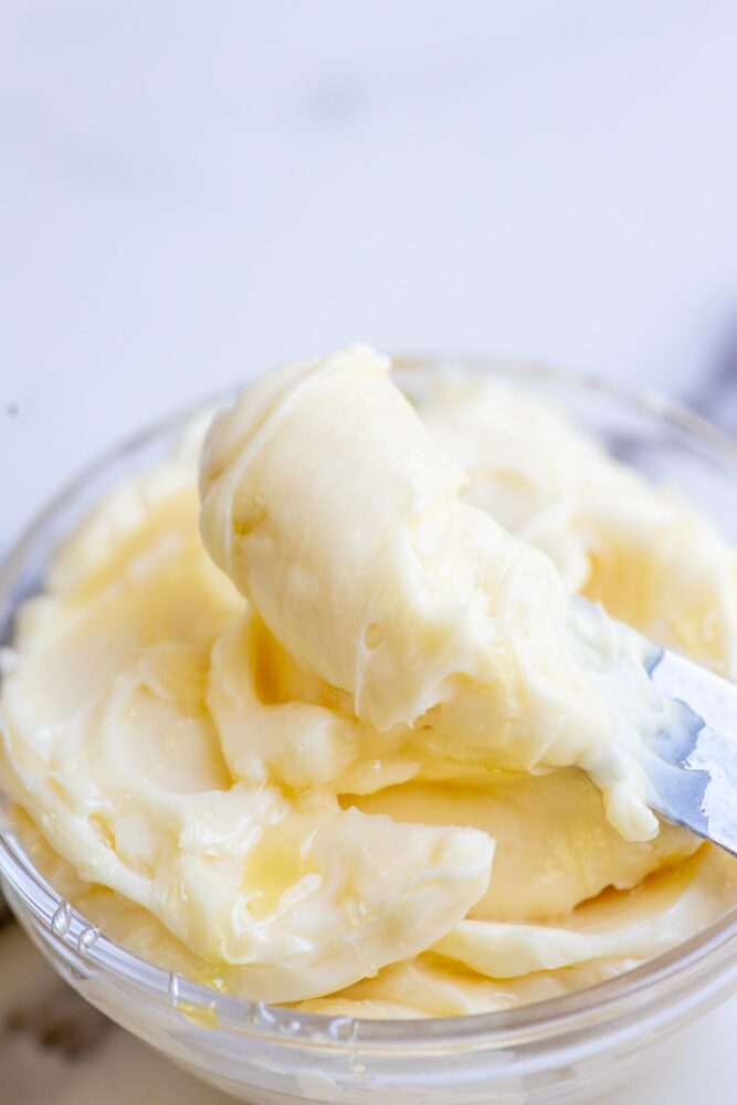 Whipped honey butter being scooped out with a knife from a glass bowl.