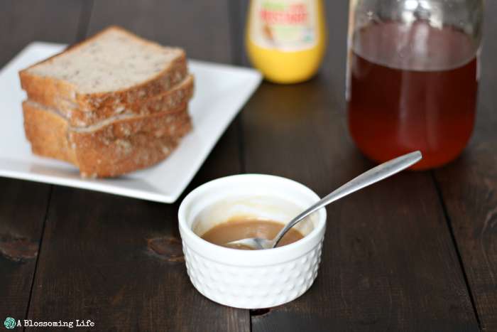 homemade honey mustard in a white dish with bread , honey, and mustard in the background