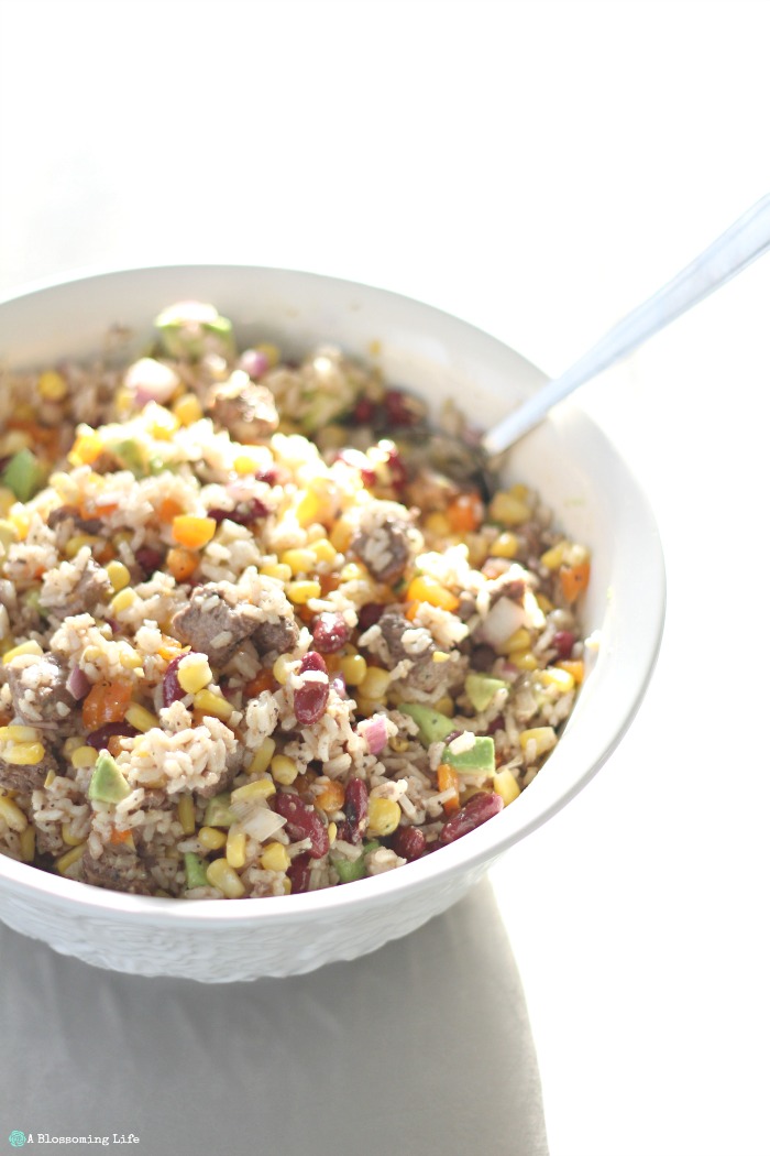 Steak and rice salad with bell pepper, corn, beans, avocado and more in a large bowl with a spoon in it