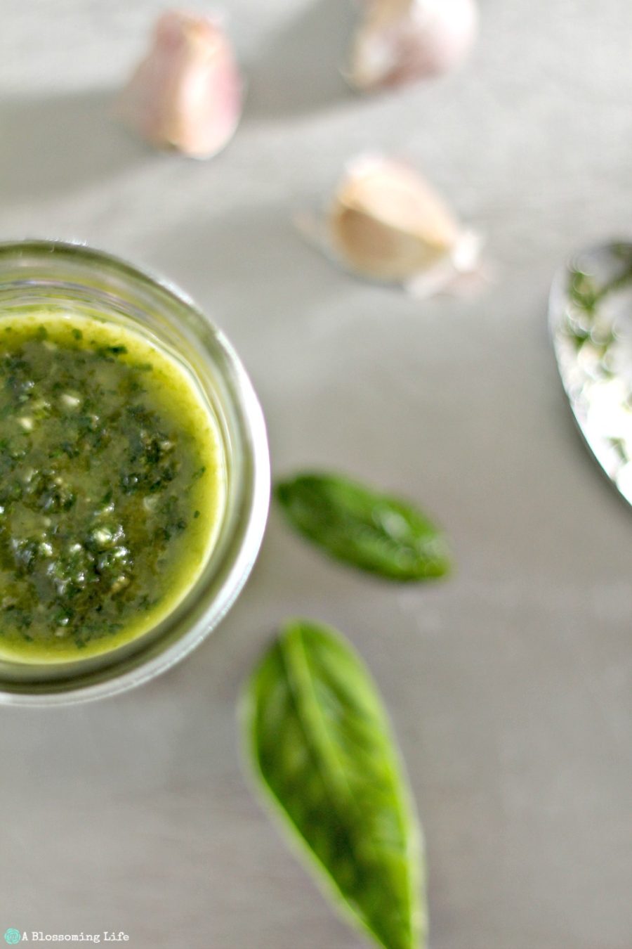 half of vegan pesto in a jar with basil and garlic cloves to the right