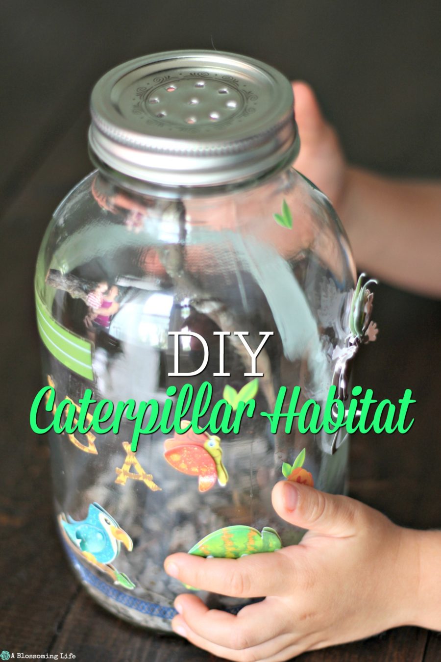 kid hands holding a DIY Caterpillar Habitat made from a mason jar and covered with stickers