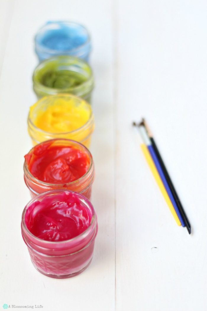 homemade finger paints in glass jars with paint brushes to the side