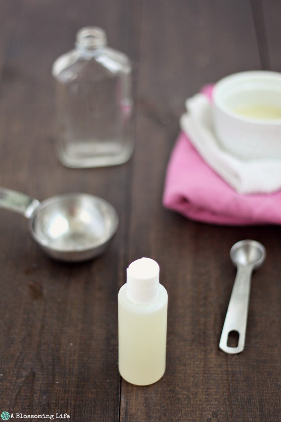 DIY hand sanitizer in a plastic container on a wood table with measuring cups around