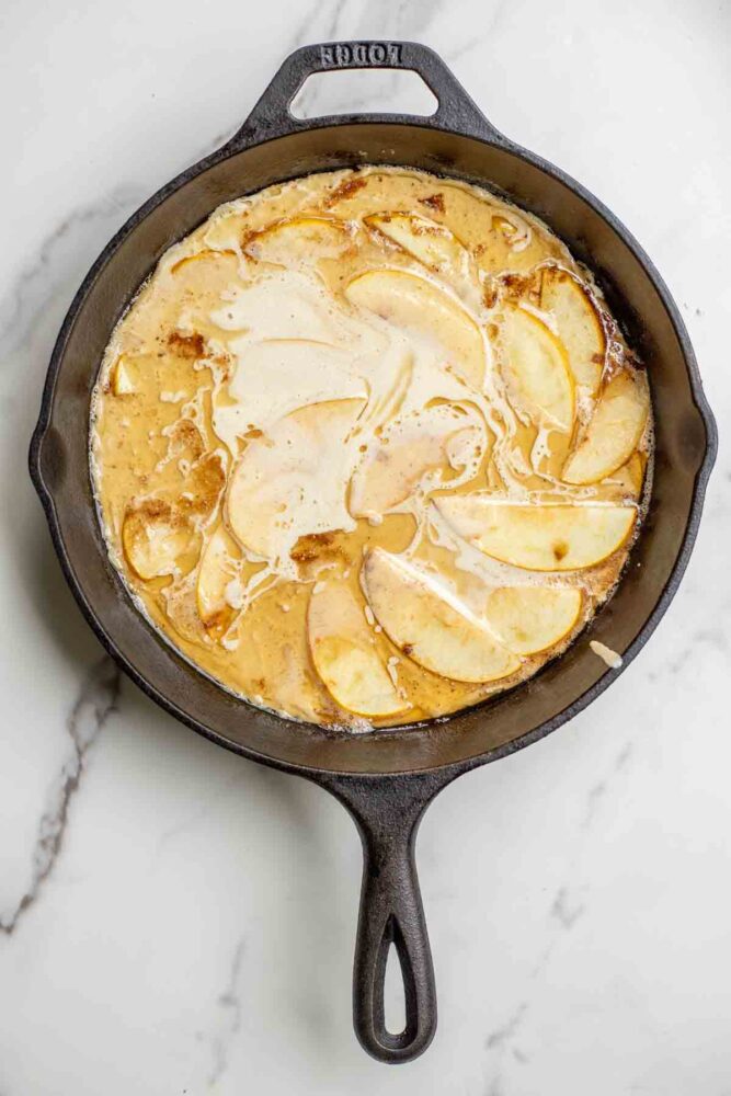 Batter poured on top of the apples in a cast iron skillet.
