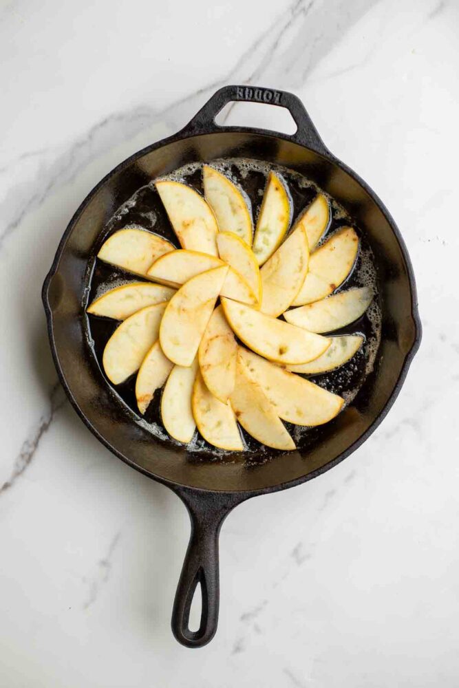 Apples placed on a buttered cast iron skillet.