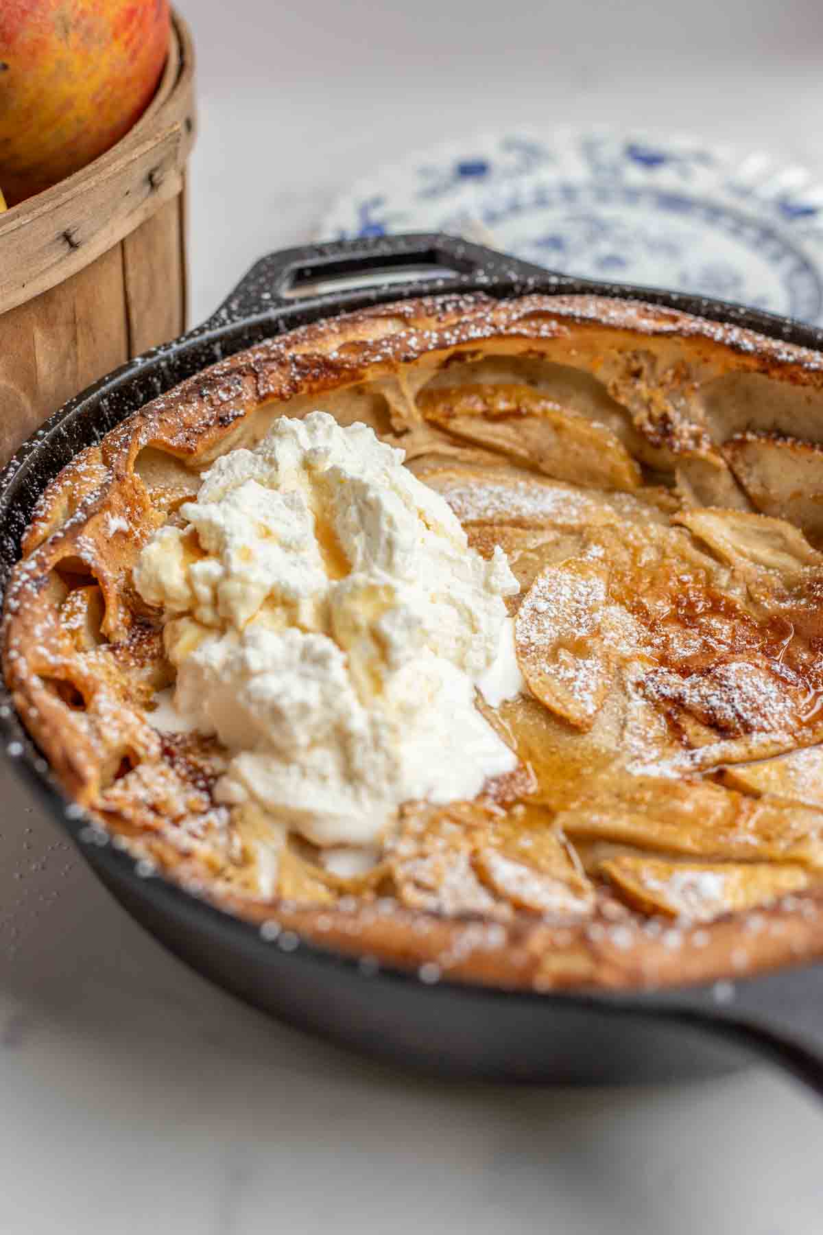 German apple pancake in a cast iron skillet, topped with maple whipped cream and maple syrup