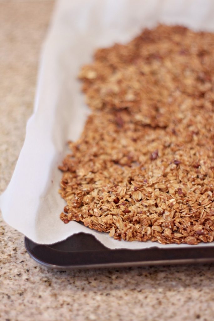 Baked homemade granola on a parchment lined baking sheet.