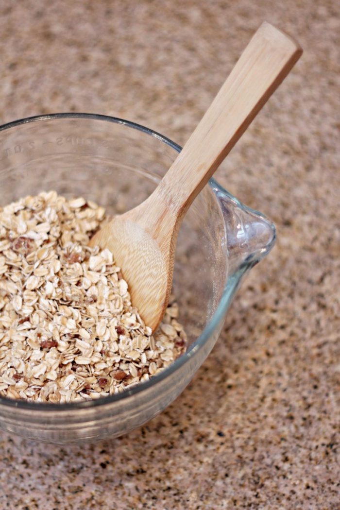 oats in a glass bowl with a wooden spoon for step by step pictures of making homemade granola