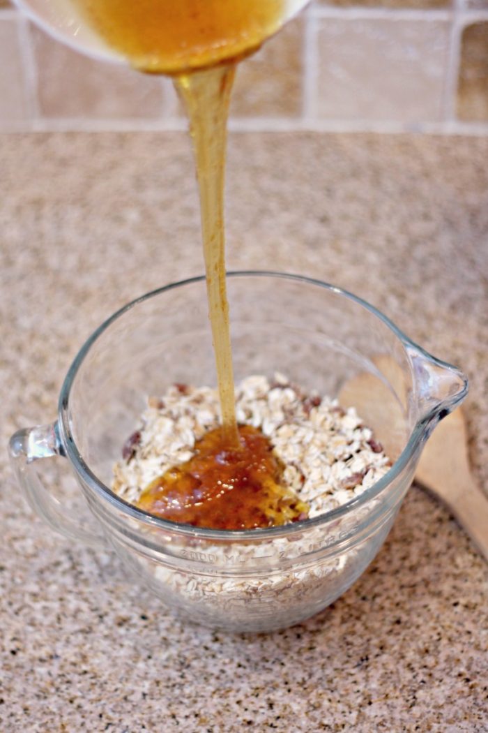 pouring honey on rolled oats in a glass bowl on a granite counter