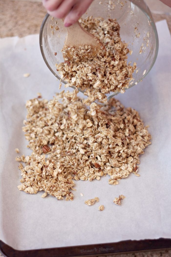 pouring granola on a parchment lined baking sheet