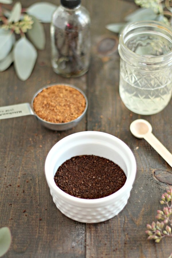 ingredients to make DIY Coffee Scrub -bowl of coffee grounds, jar of coconut oil, tbs of coconut sugar, eucalyptus, and a jar of vanilla beans in the background.