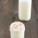 glass of frothy homemade eggnog topped with freshly grated nutmeg with a jar of eggnog in the background