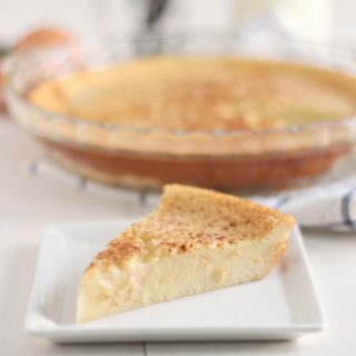 slice of custard pie on a white dish with the whole pie behind it on a white and blue towel