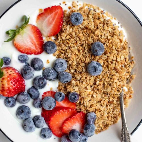 A white bowl filled with yogurt topped with homemade healthy granola, strawberries, and blueberries.