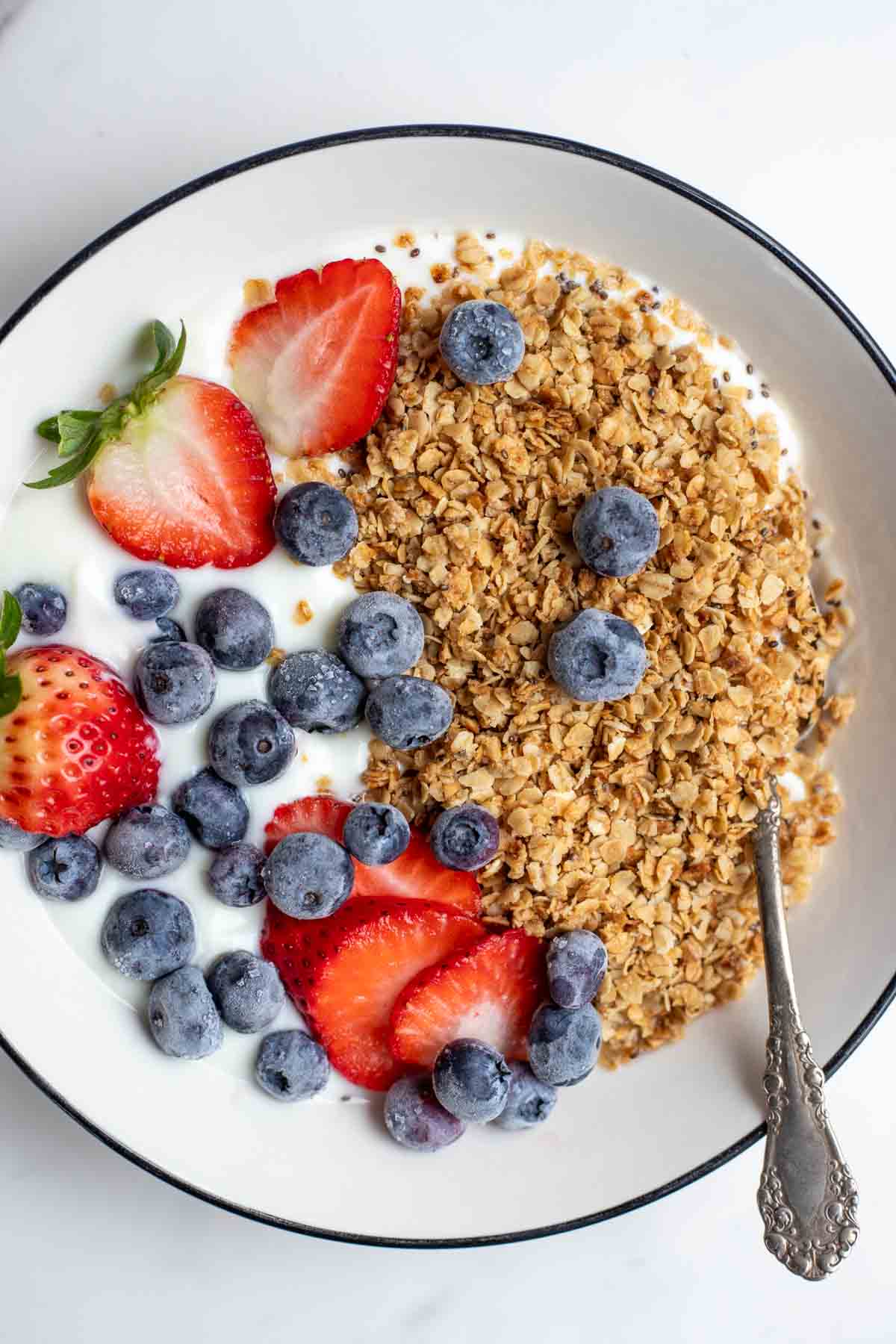 A white bowl filled with yogurt topped with homemade healthy granola, strawberries, and blueberries.