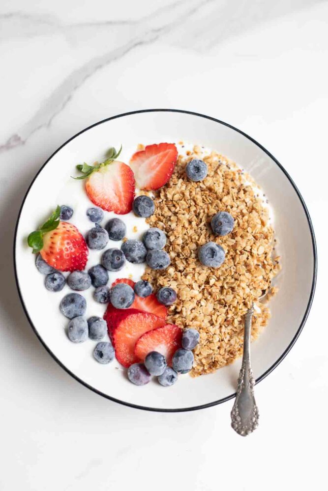 Overhead photo of a bowl of yogurt topped with homemade granola, slice strawberries and blueberries.