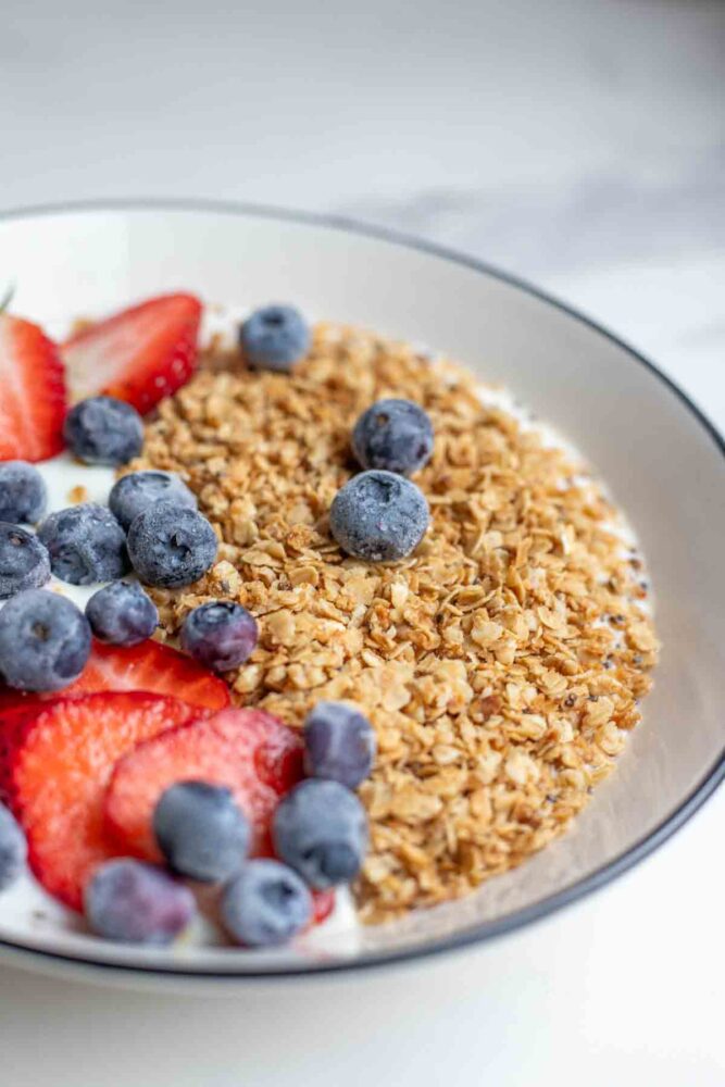 Side view of a bowl filled with yogurt, healthy granola, blueberries and strawberries.