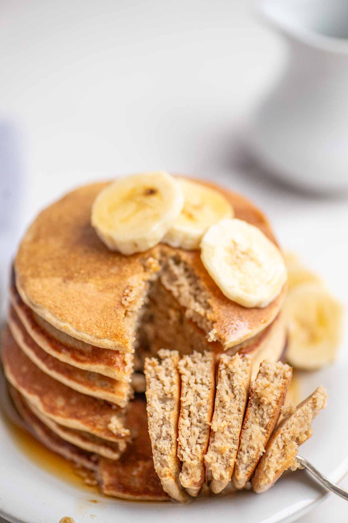 Banana oat pancakes topped with sliced bananas and maple syrup with a slice of pancake on a fork.