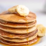 Close up of a stack of oatmeal banana pancakes topped with maple syrup and sliced bananas.