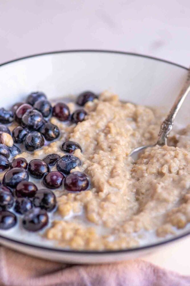 Bowl of oatmeal custard topped with blueberries, maple syrup and cream.