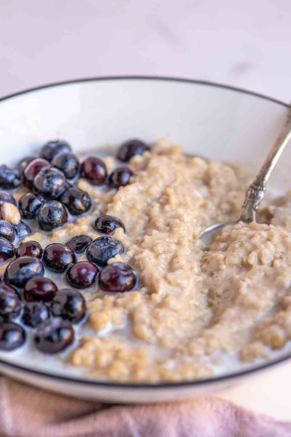 Bowl of oatmeal custard topped with blueberries, maple syrup and cream.