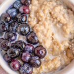 Overhead photo of custard oatmeal topped with blueberries and cream.