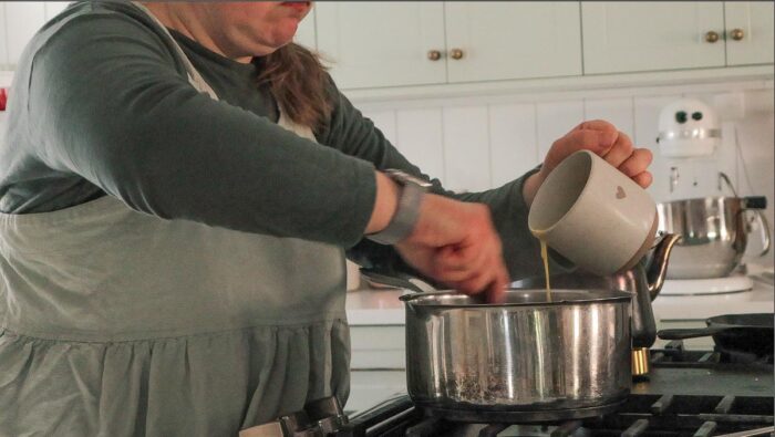 Slowing adding tempered eggs to a pot of hot oatmeal.
